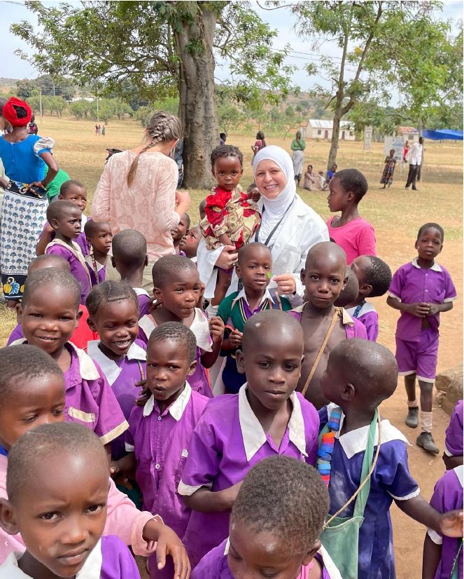 Sura Hadad is smiling surrounded by a group of children and holds one in her arms in Africa.